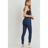 Rear view of high rise dark denim skinny jeans modeled by woman in black top and white tennis shoes