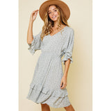 Blonde model wearing a ruffle v-neck dress with a sage and white daisy floral print paired with a tan suede hat