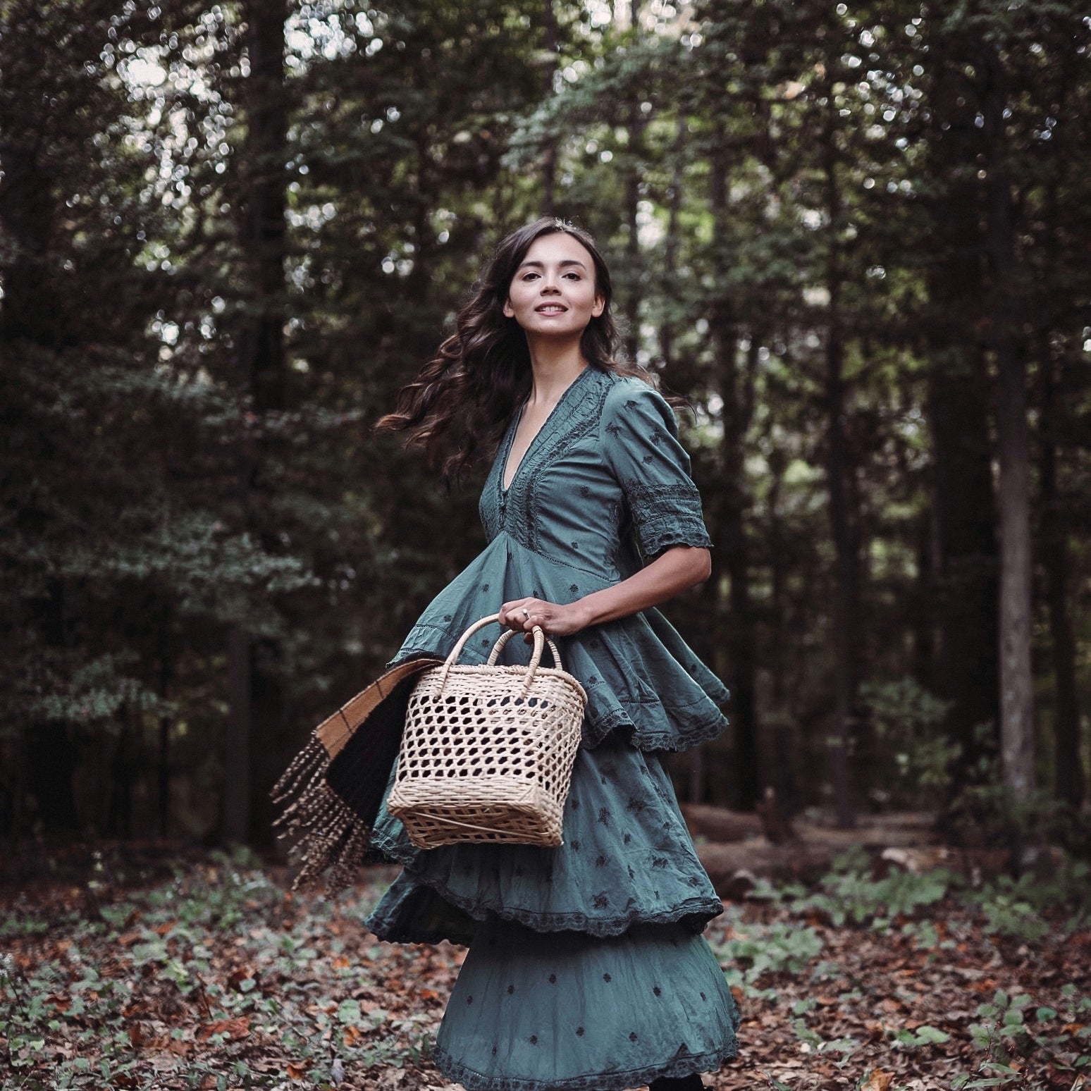 Model wearing a blue gown in the woods holds the small talia woven straw basket