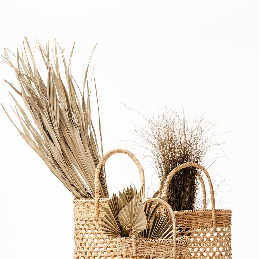 Small, medium, and large talia woven straw baskets are shown filled with muted greenery against a white background