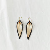 Pair of two-tone black and gold metallic leather earrings in the shape of an upside-down teardrop in front of a white backdrop