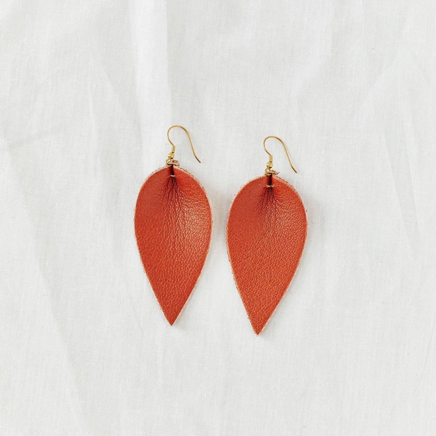 Pair of blood orange leather earrings in the shape of an upside-down teardrop in front of a white backdrop