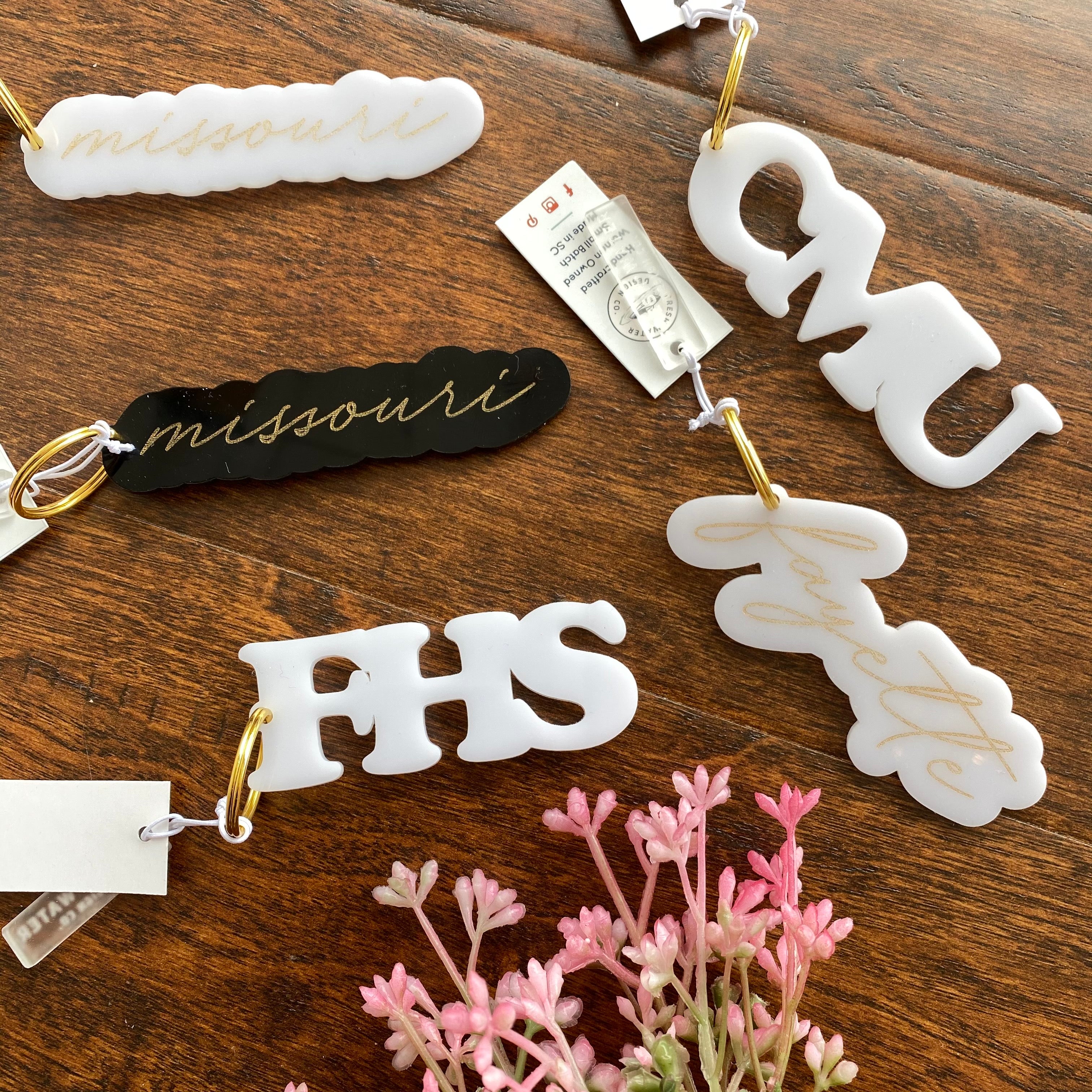 White missouri, black missouri, CMU, FHS, and Fayette acrylic keychains sit together on wood surface with pink florals