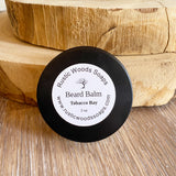 Black canister jar with white rustic woods soaps tobacco bay beard balm label leans against wood pieces