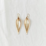 Pair of two-tone cream and metallic gold leather earrings in the shape of an upside-down teardrop in front of a white backdrop