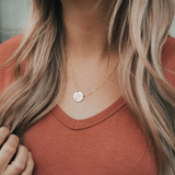 Model wearing gold circle necklace paired with a rust colored shirt and wavy hair
