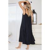 Back view of blonde model posing in a black pleated midi dress with spaghetti straps in a bright white shabby chic room
